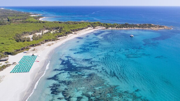 Luchtbeeld van een strand met helder turquoise water, een zandstrand en een rij parasols.