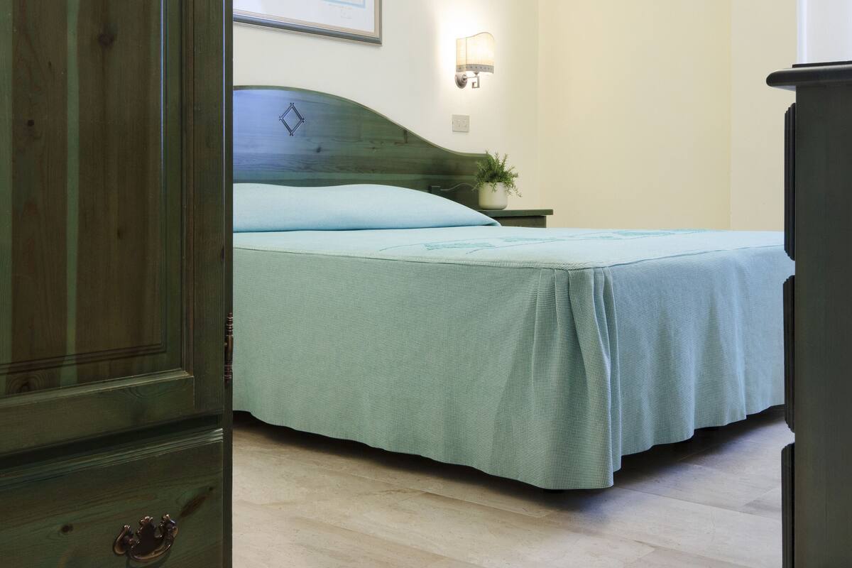 A bedroom with a bed, a nightstand, a wall-mounted lamp, and a ceiling light.