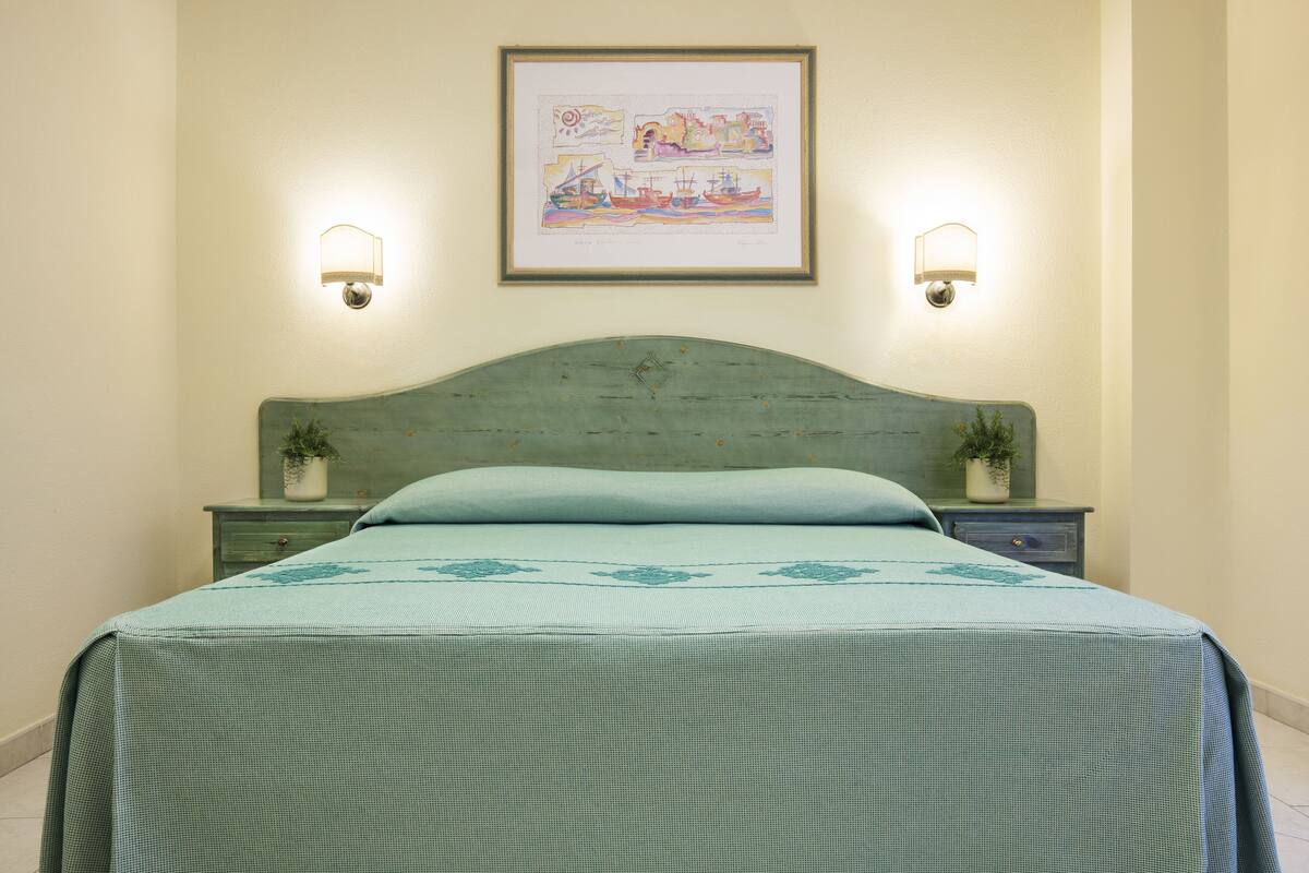 A neatly made bed with a checkered bedspread, two bedside tables with lamps, and a framed artwork above the bed.