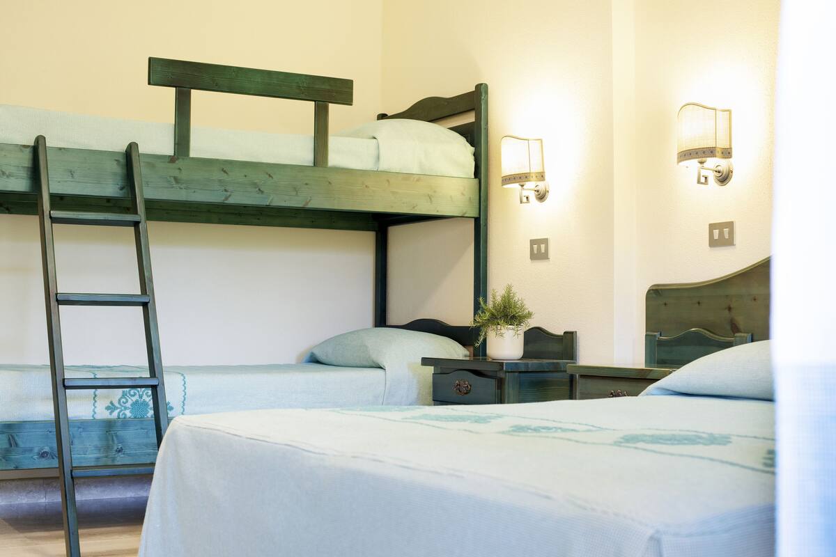 A bunk bed room with a ladder, bedside tables, and wall-mounted lights.