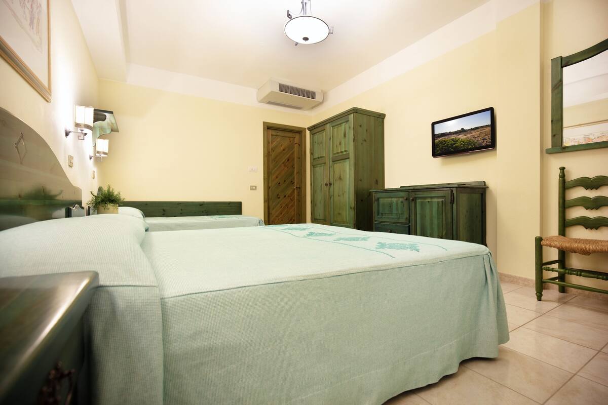 A bedroom with two beds, a wooden wardrobe, a television, and a framed picture on the wall.