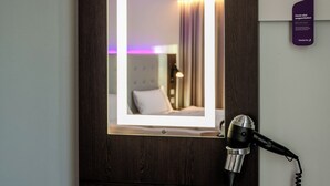 A hotel room with a mirror, a hairdryer, and a phone on a wooden counter.