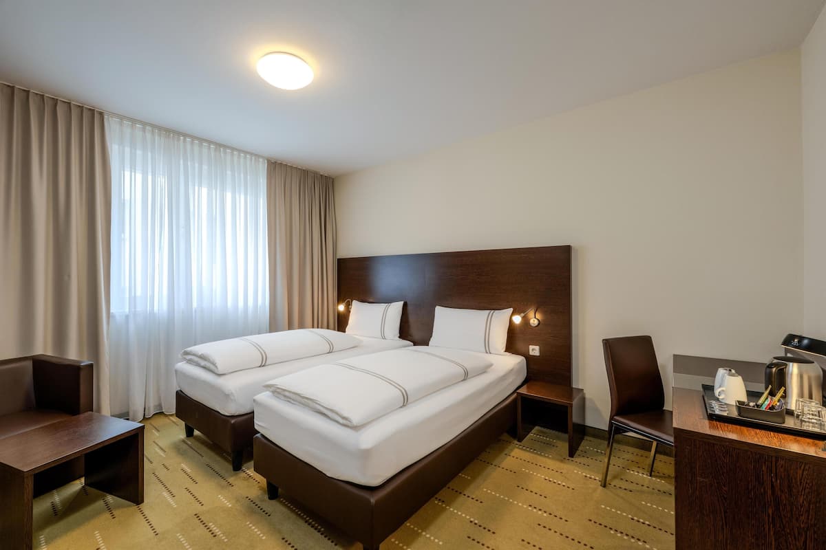 A hotel room with two beds, a desk, a chair, and a coffee maker.