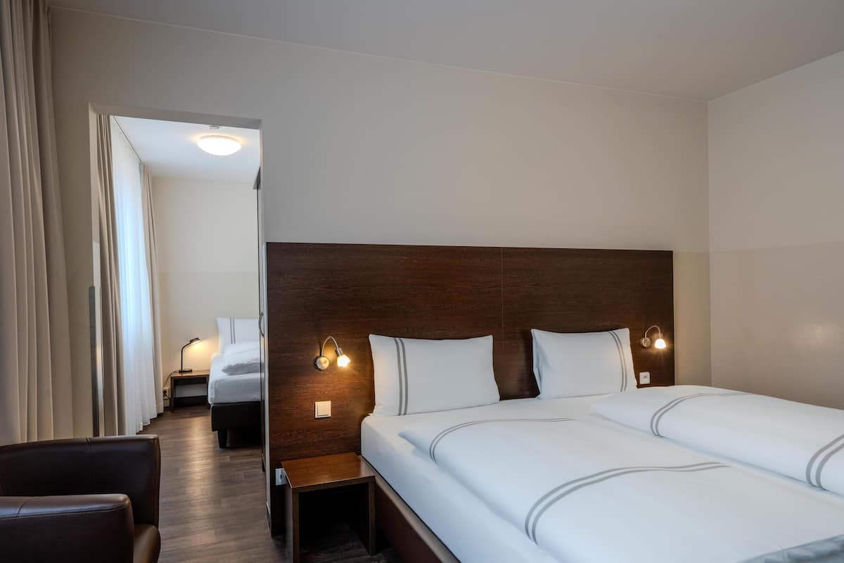 A hotel room with a large bed, bedside lamps, a chair, and a wooden headboard.