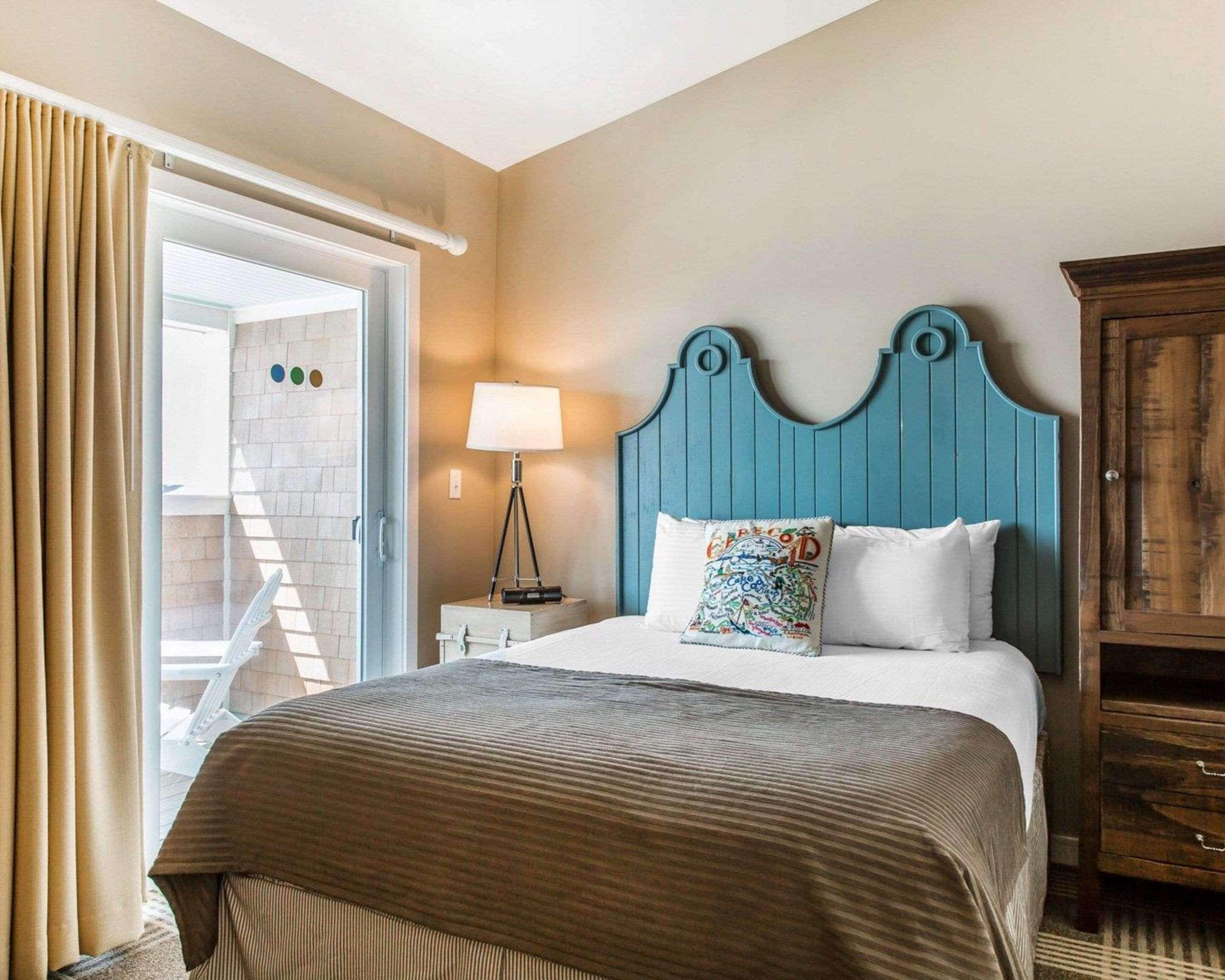 A hotel room with a bed, a nightstand with a lamp, a wooden headboard, and a wardrobe.