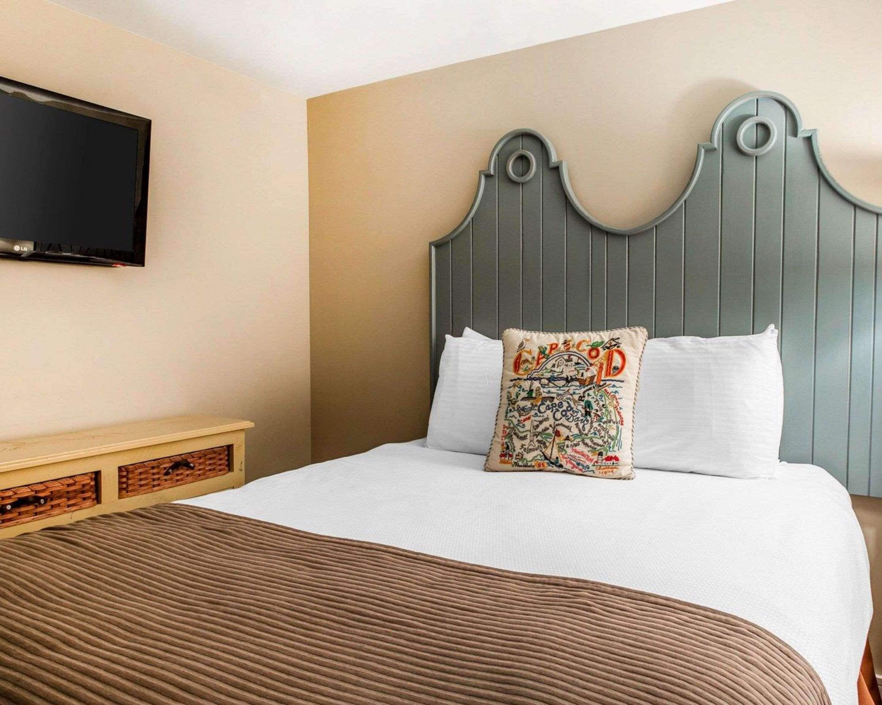 Una cama bien hecha con un edredón marrón, un cabecero gris y dos almohadas, una con un diseño colorido.