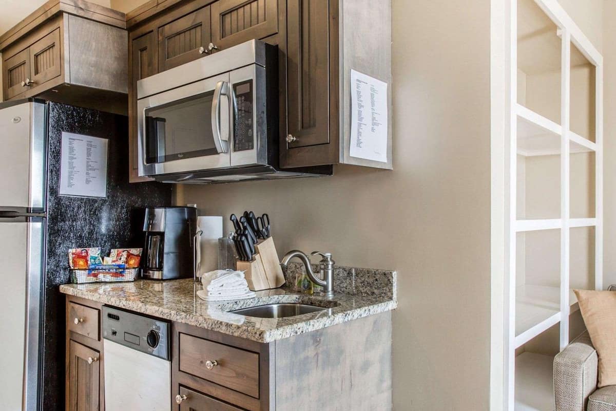 A kitchen with dark wooden cabinets, a stainless steel microwave, a coffee maker, and a sink with a knife block.