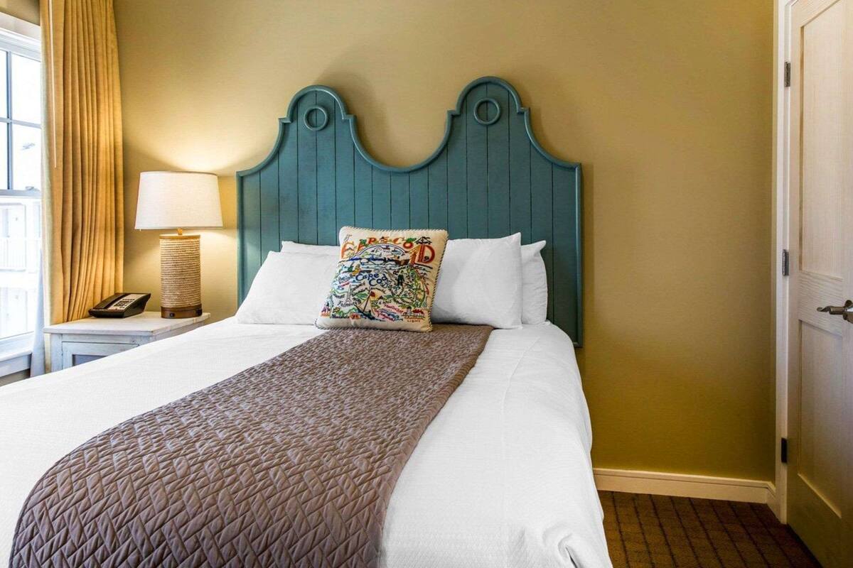 A neatly made bed with a quilted brown blanket, a decorative pillow, and a teal headboard.