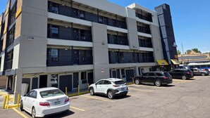 Un parking à plusieurs étages où sont garées plusieurs voitures, un bâtiment à la façade plate et un ciel bleu dégagé.