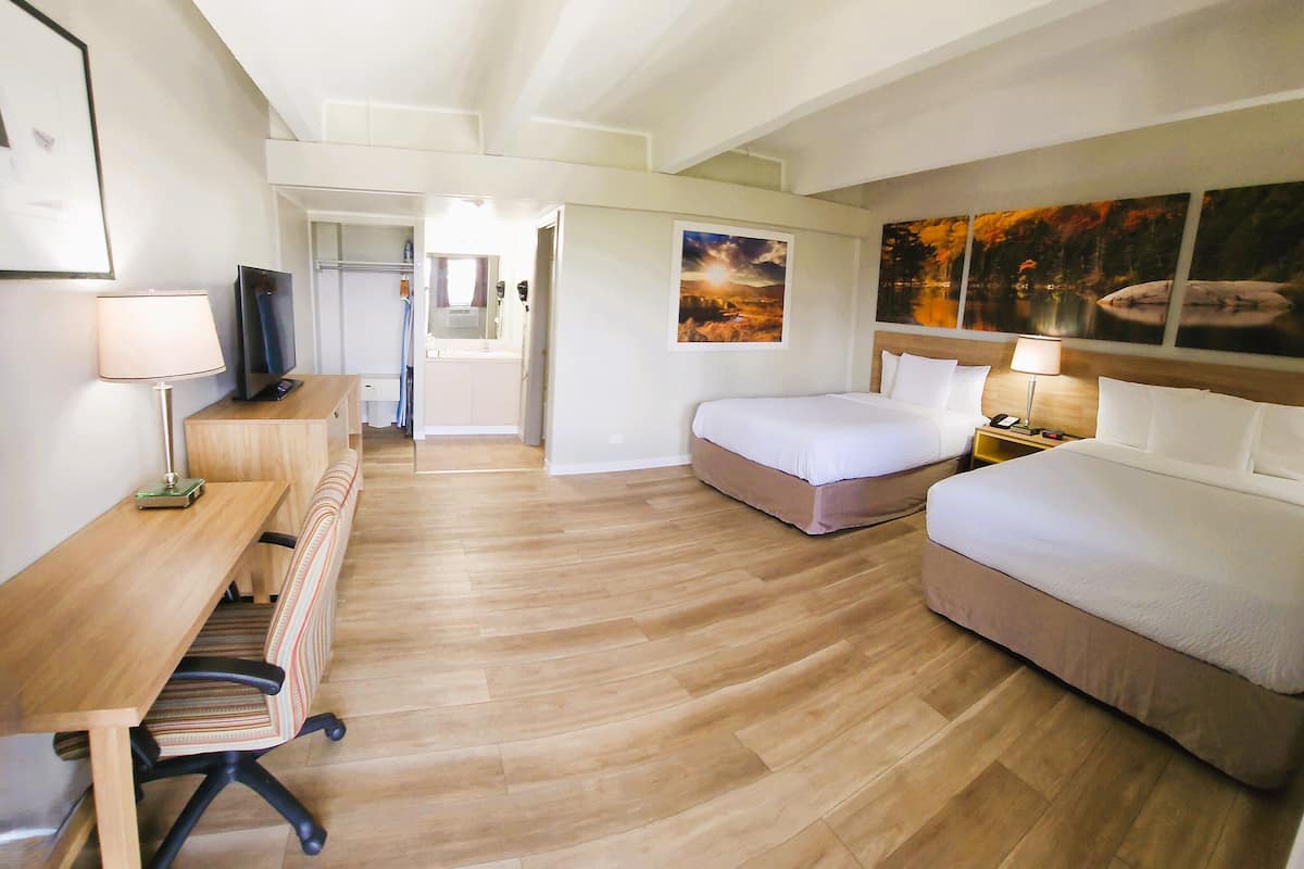 A hotel room with two beds, a desk, a chair, a TV, and artwork on the walls.