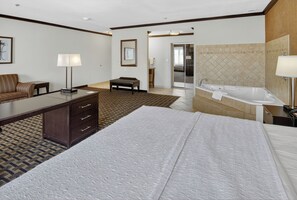 A hotel room with a bed, a desk, a chair, a bench, a bathroom with a bathtub, and a sliding door leading to another room. - Hampton Inn & Suites Longview North (Longview)