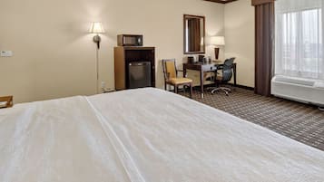 Habitación de hotel con cama, escritorio, silla, microondas, refrigerador y una ventana grande.
