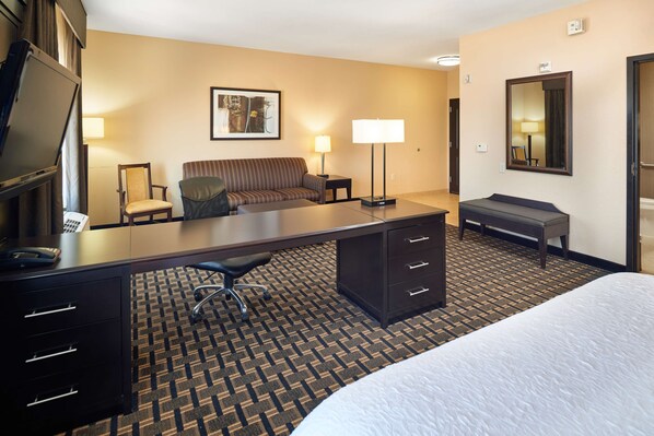 A hotel room with a bed, desk, chair, sofa, and two lamps.