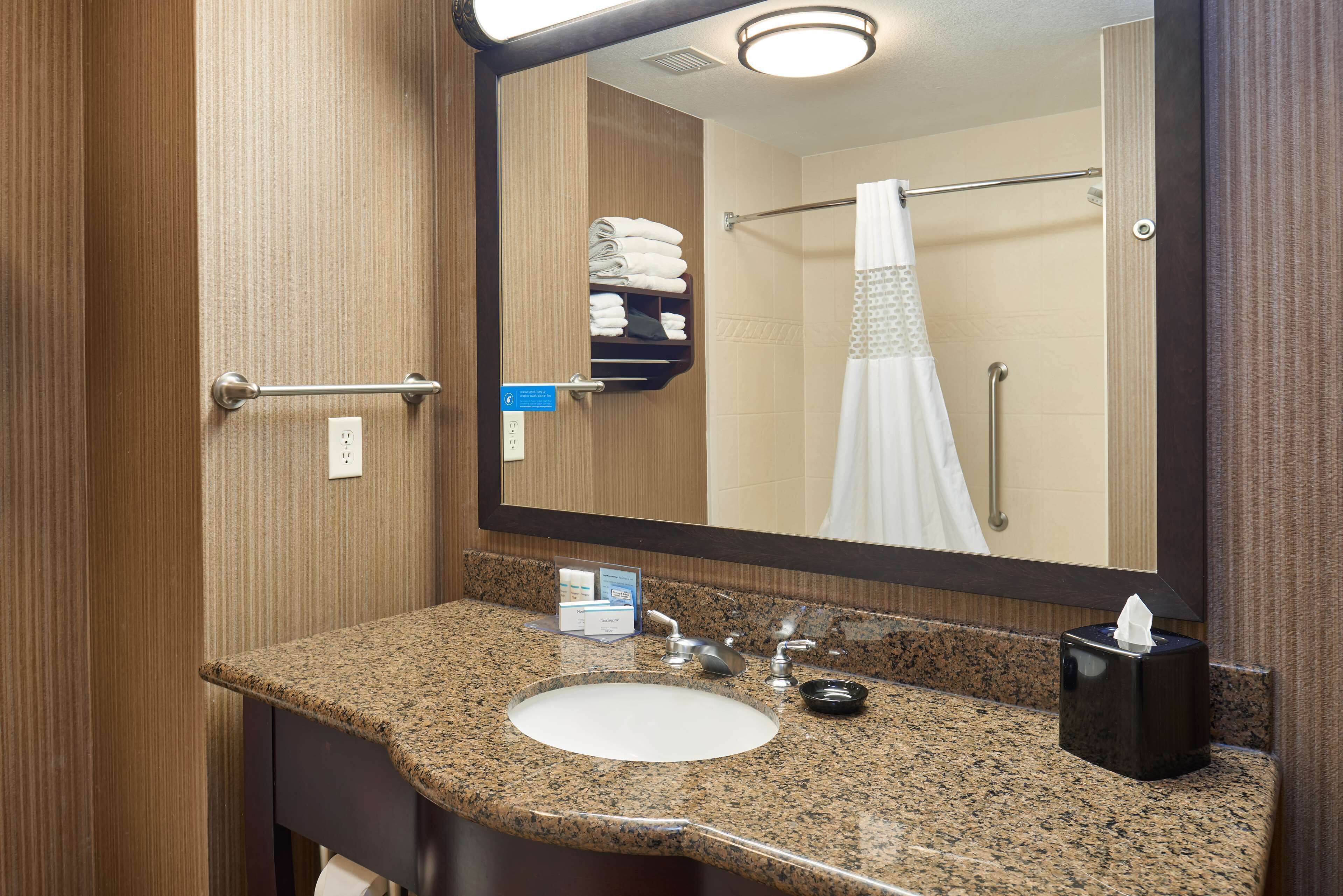 A bathroom with a granite countertop sink, a mirror, a towel rack with folded towels, and a tissue box.