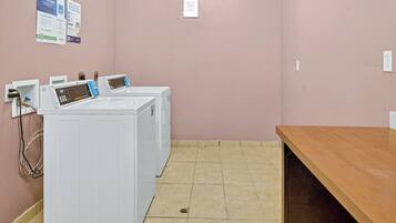Un espace buanderie comprenant deux machines à laver blanches, un banc en bois et un panneau fixé au mur.