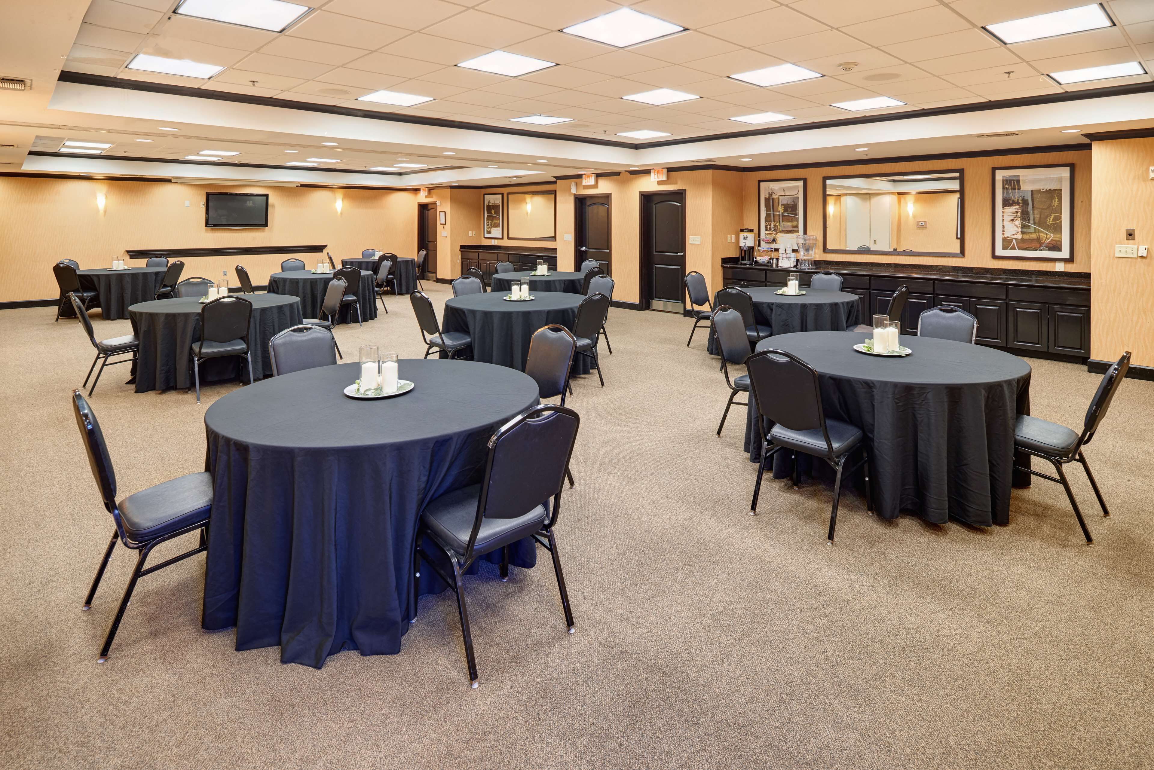 A conference room with multiple round tables, each surrounded by chairs, and a large screen on the wall.