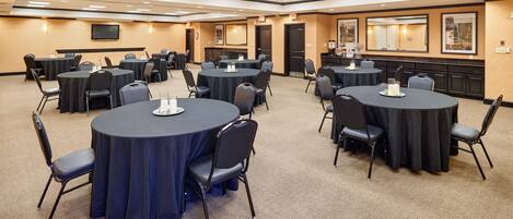 A conference room with multiple round tables, each surrounded by chairs, and a large screen on the wall.