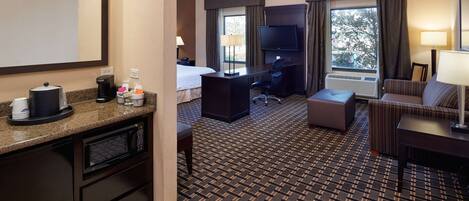 A hotel room with a bed, desk, and seating area. It includes a microwave, coffee maker, and a television.