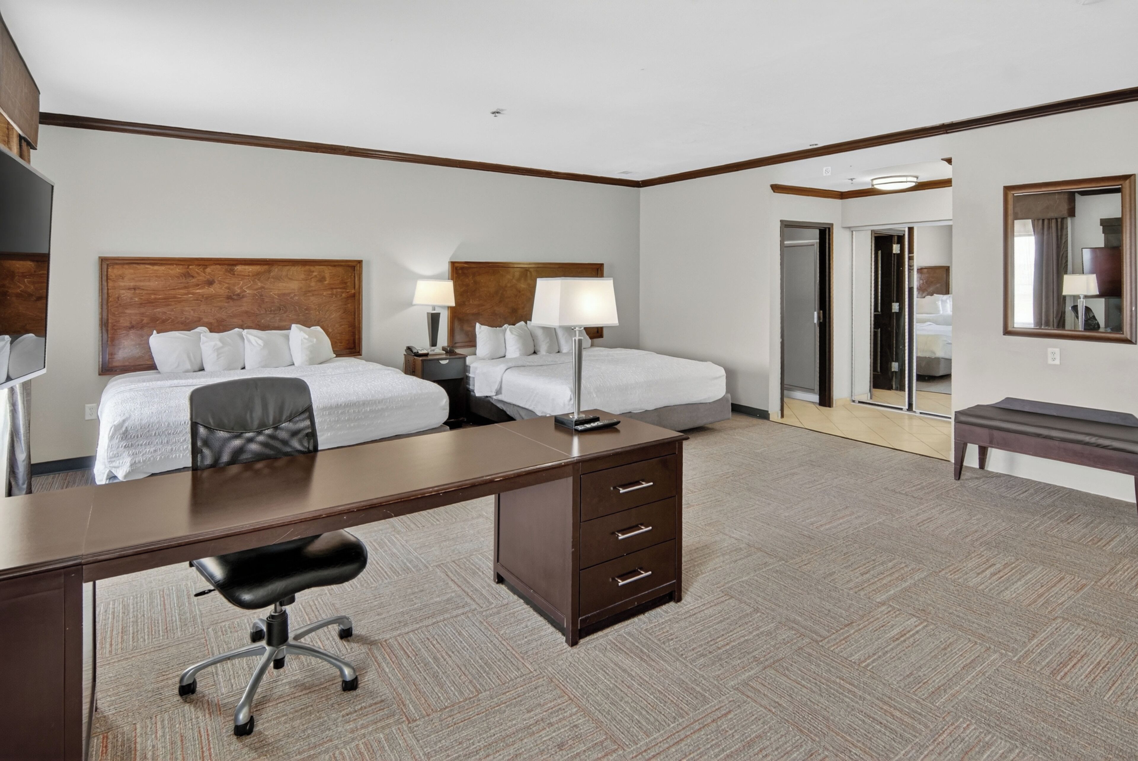 A hotel room with two beds, a desk, a chair, a dresser, and a mirror.