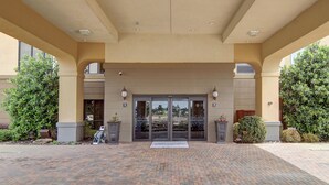 A hotel entrance with a brick-paved driveway, double doors, and a covered waiting area.