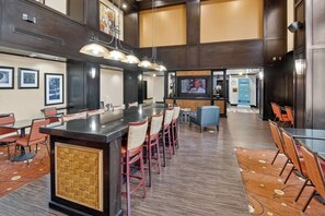 A spacious hotel lobby with a long bar, multiple seating areas, and a television screen. - Hampton Inn & Suites Longview North (Longview)