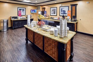 A hotel breakfast area with a buffet counter, microwave, and various food items.