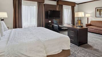 Quarto de hotel com cama grande, escrivaninha com cadeira, televisão e sofá.