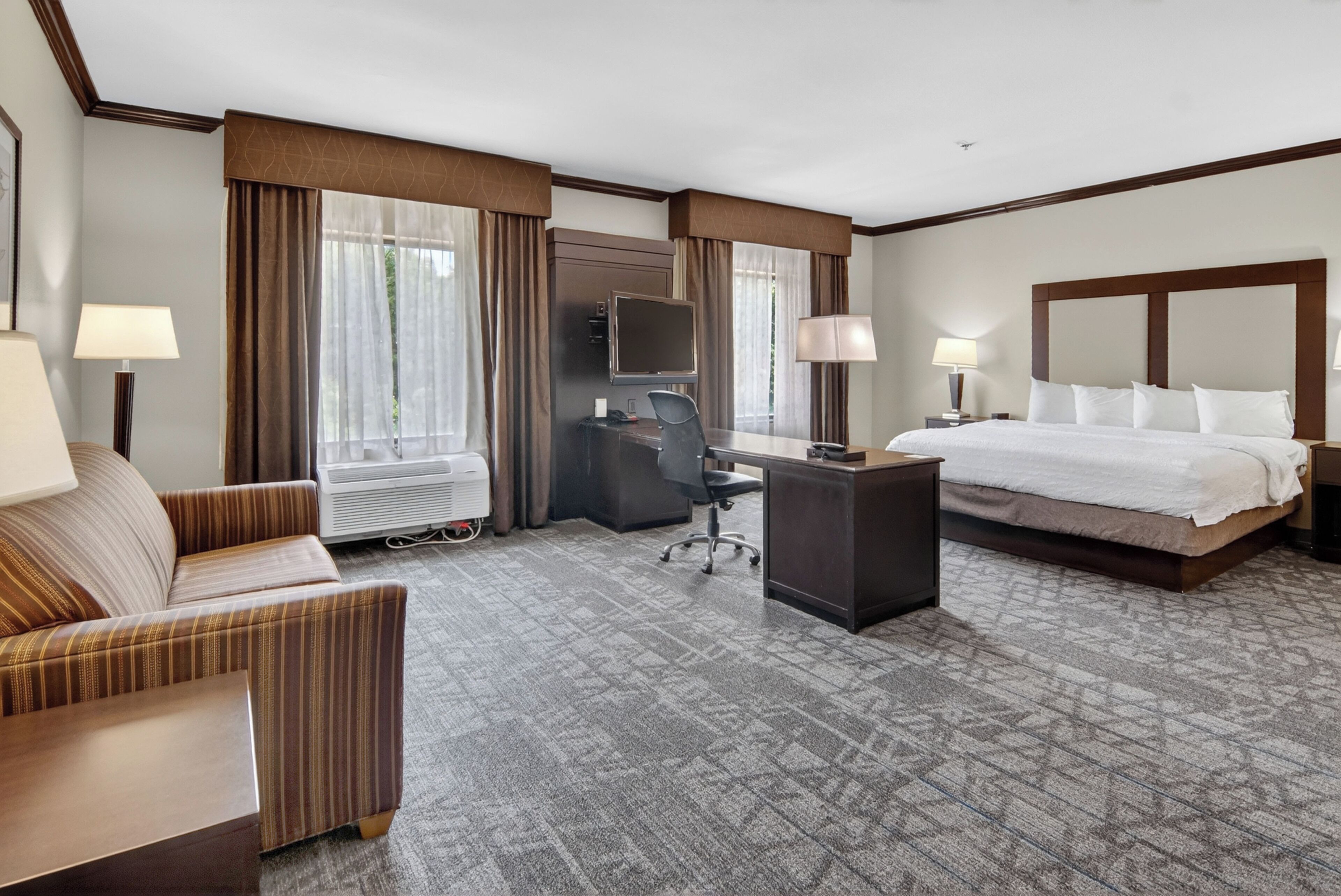 A hotel room with a bed, a desk, a chair, a TV, and a lamp.