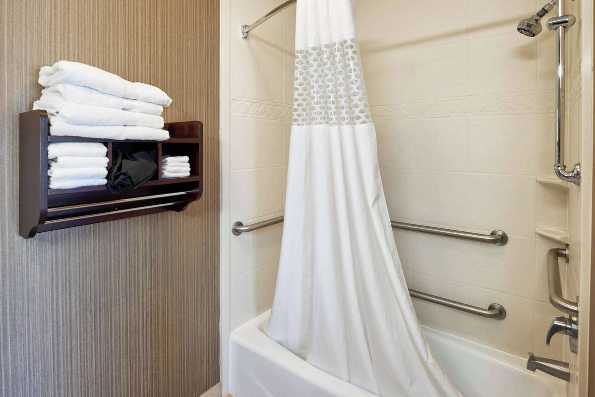 A bathroom with a white bathtub, a towel rack with folded towels, and a shower curtain with a perforated section.