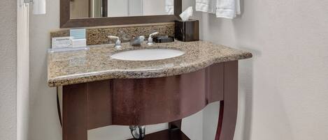 Un baño con lavabo de encimera de granito, espejo, toallero y dispensador de jabón.