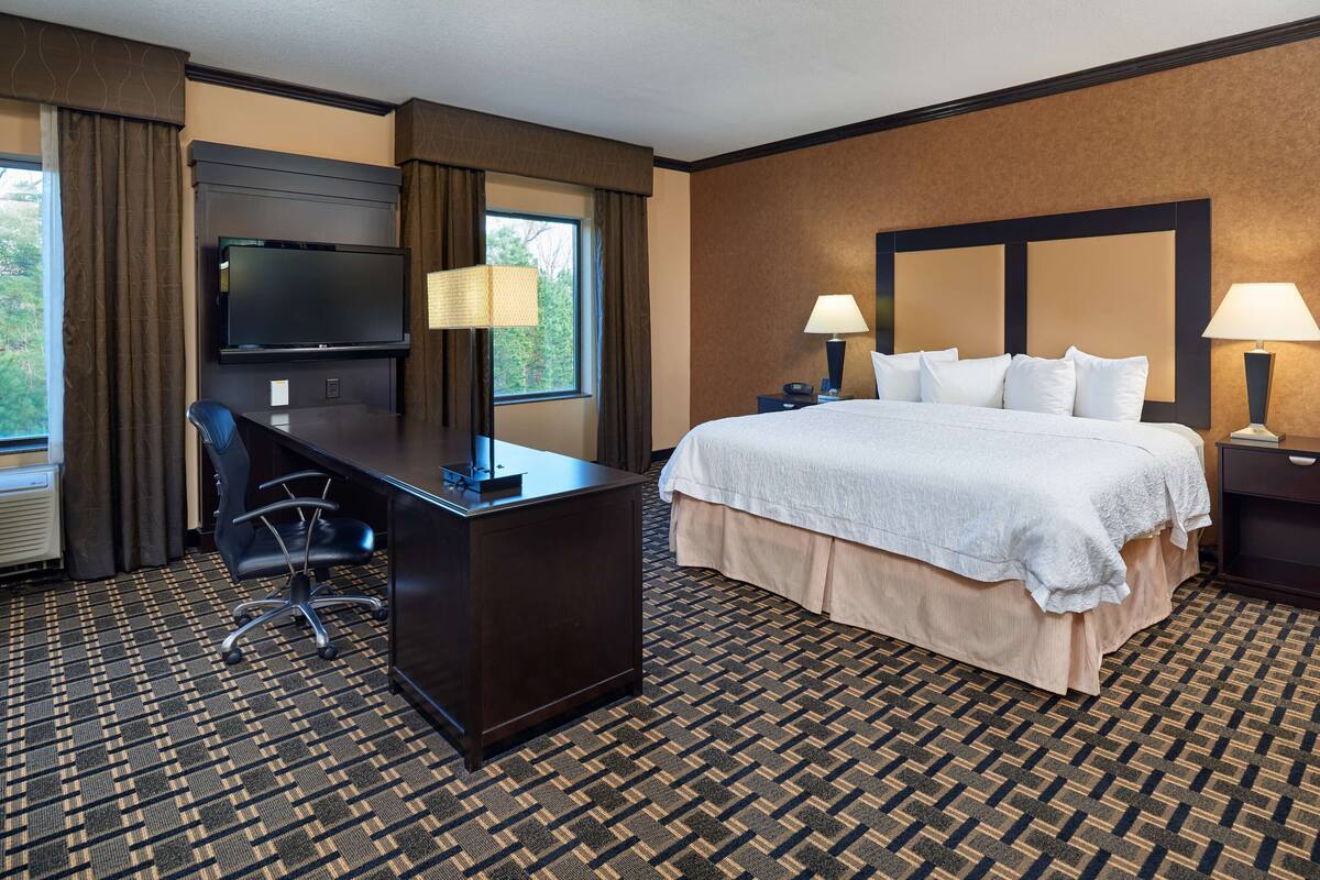 A hotel room with a large bed, a desk with a chair, a flat-screen TV, and two bedside lamps.
