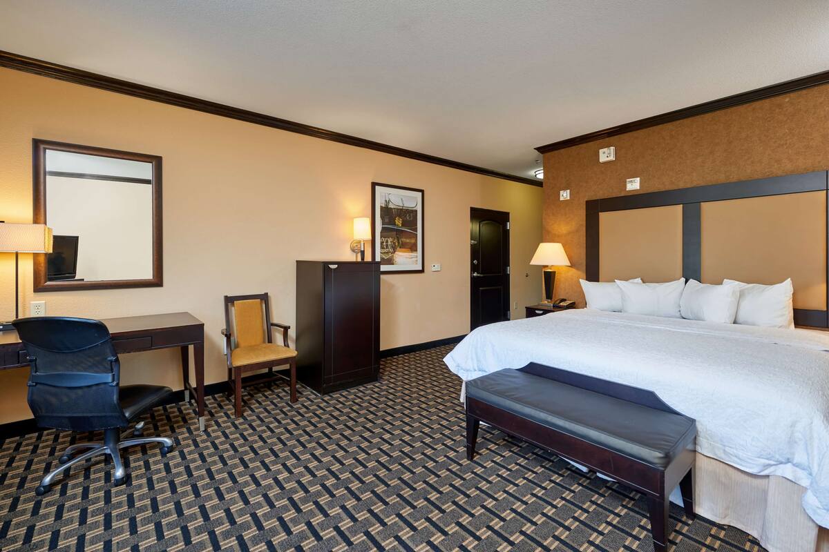A hotel room with a bed, desk, chair, and a large mirror.