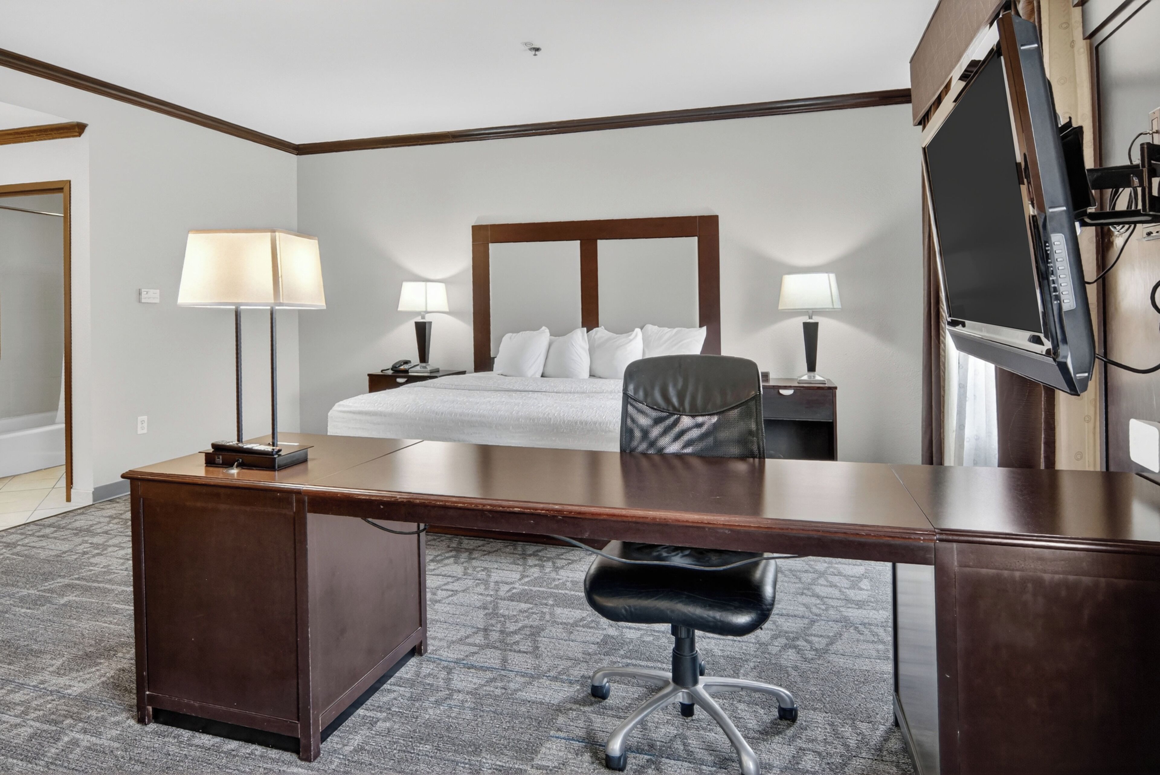 A hotel room with a large bed, a desk, two lamps, a chair, and a TV.