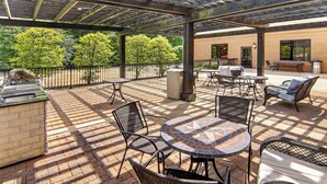 Un patio al aire libre con una parrilla, muebles de mimbre y vistas a árboles.