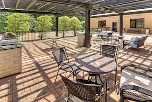 Un patio al aire libre con una parrilla, muebles de mimbre y vistas a árboles.