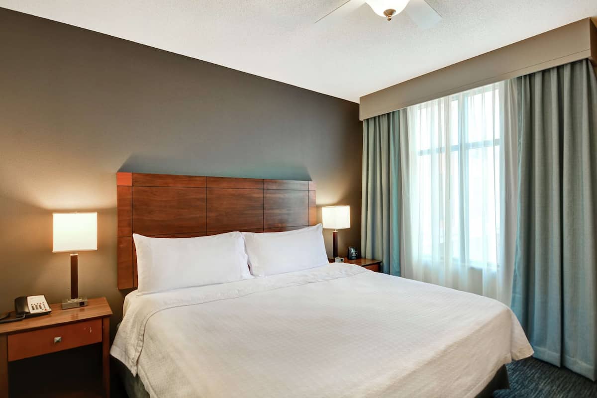 A hotel room with a large bed, two bedside lamps, a nightstand with a phone, and a window with curtains.