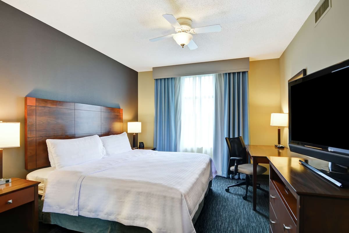 A hotel room with a large bed, a desk with a TV, a chair, and a ceiling fan.