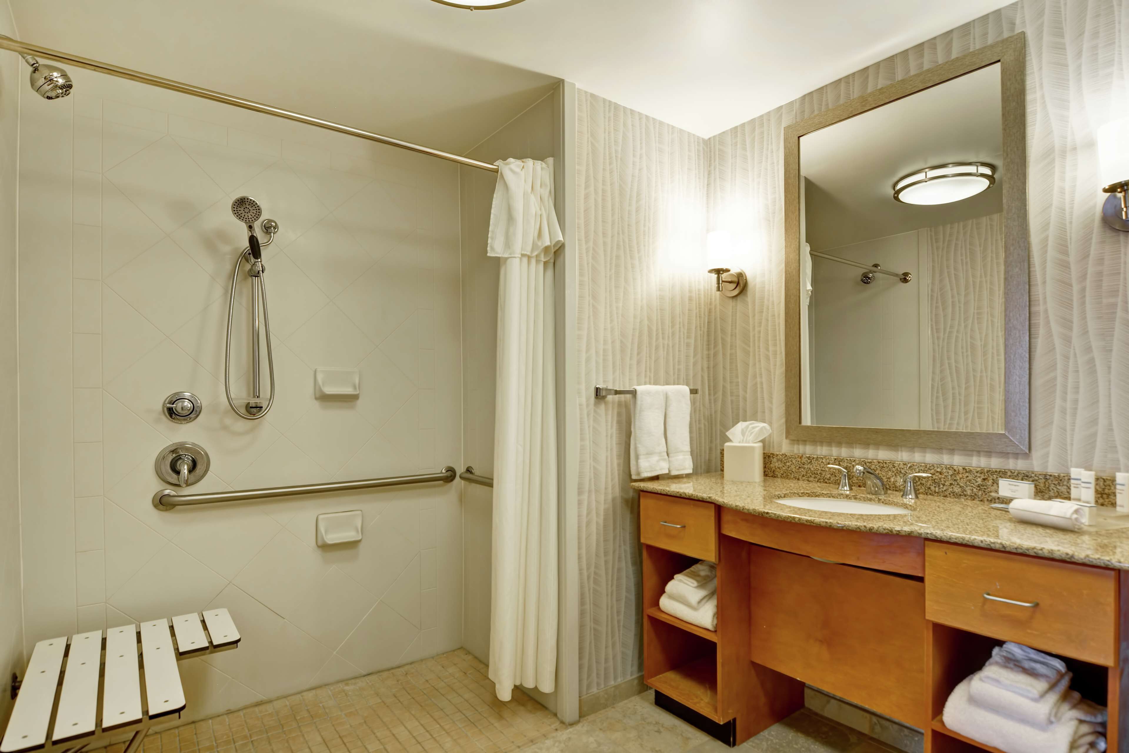 A modern bathroom with a shower, grab bars, a vanity with a sink, and a large mirror.