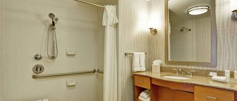 A modern bathroom with a shower, grab bars, a vanity with a sink, and a large mirror.