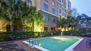 A hotel pool area with a rectangular pool, lounge chairs, and palm trees.