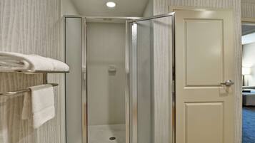 A bathroom with a glass shower enclosure, a towel rack with folded towels, and a door leading to another room.