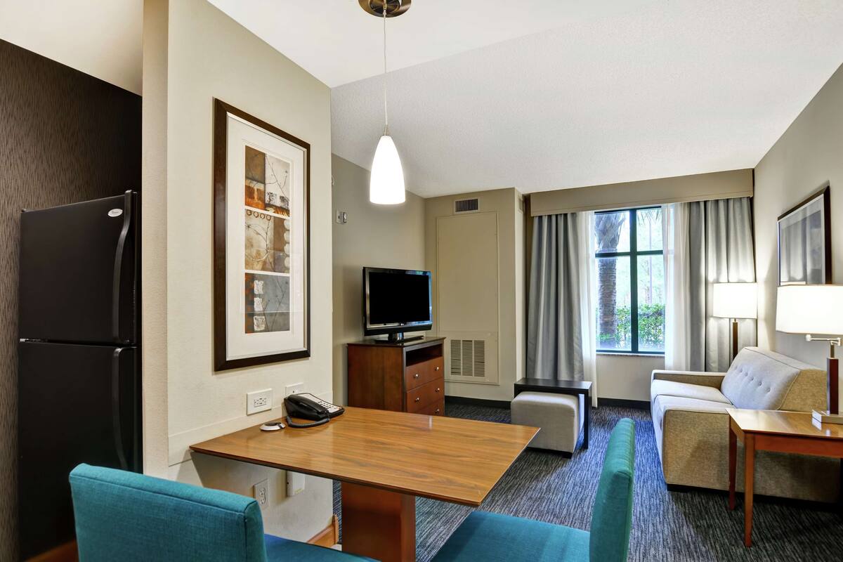 A hotel room with a wooden desk, a television, a sofa, and a dining table.