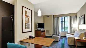 A hotel room with a wooden desk, a television, a sofa, and a dining table.