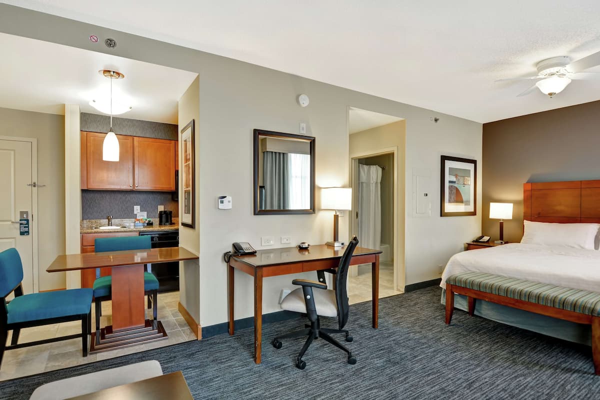 A hotel room with a bed, desk, chair, and kitchenette.