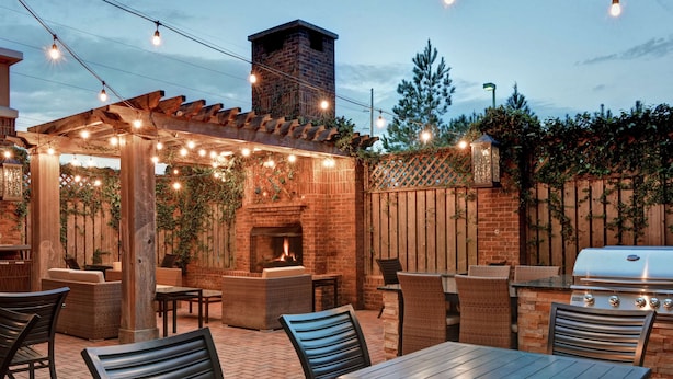 An outdoor patio with brick flooring, wooden pergola, string lights, and outdoor furniture.
