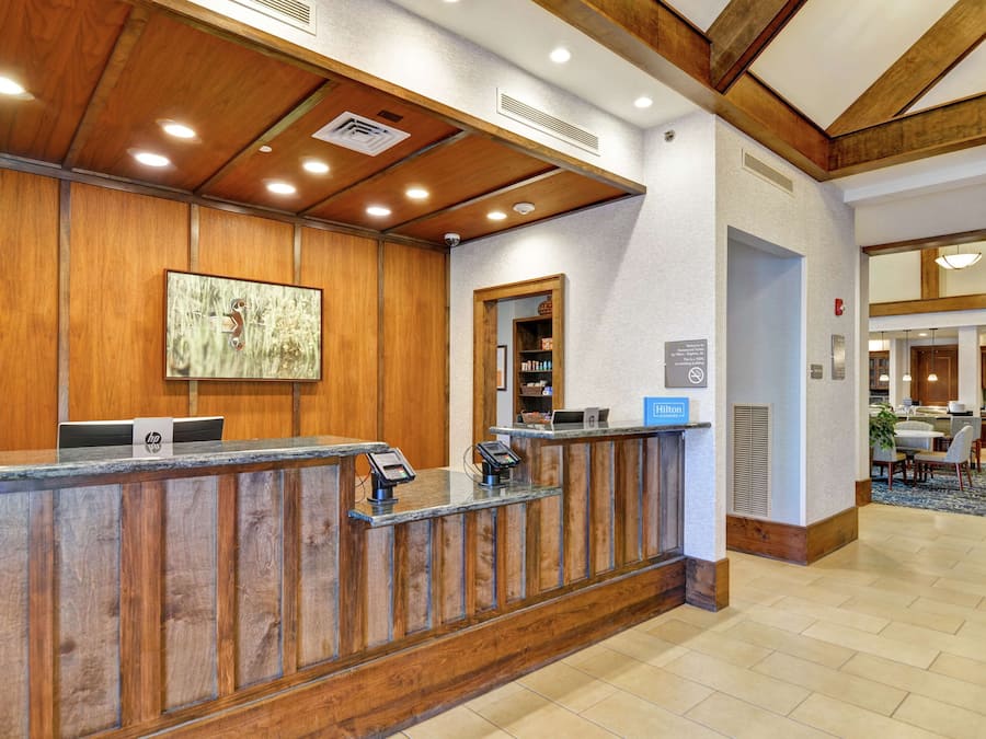 Un'area della reception di un hotel con scrivania in legno, una postazione di check-in digitale e vista sul ristorante.
