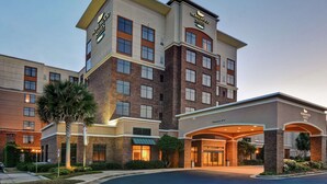 A hotel with a modern design, featuring a central entrance with a covered walkway and multiple floors with large windows.