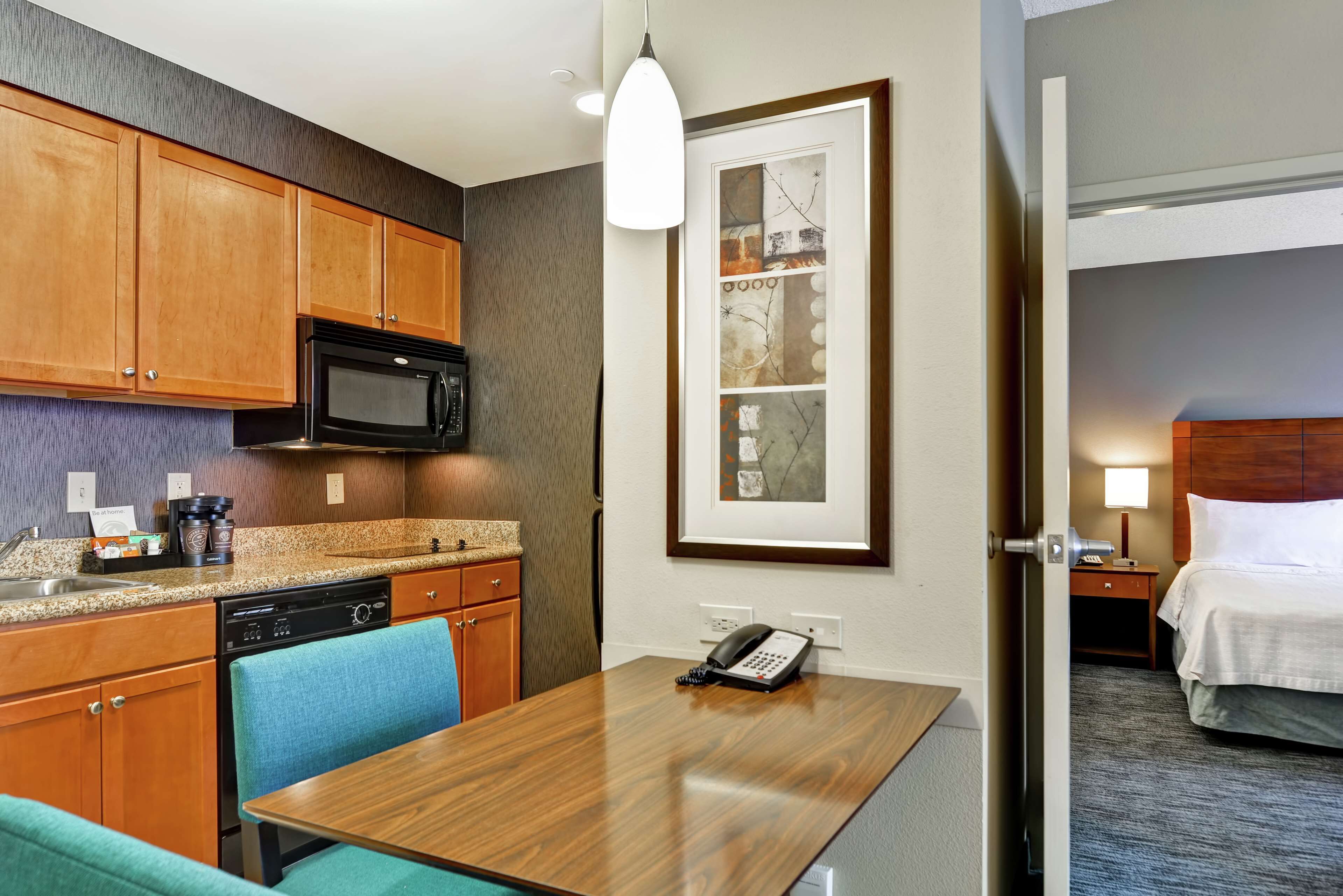 A hotel room with a kitchenette, a dining area, a bed, and a framed artwork on the wall.