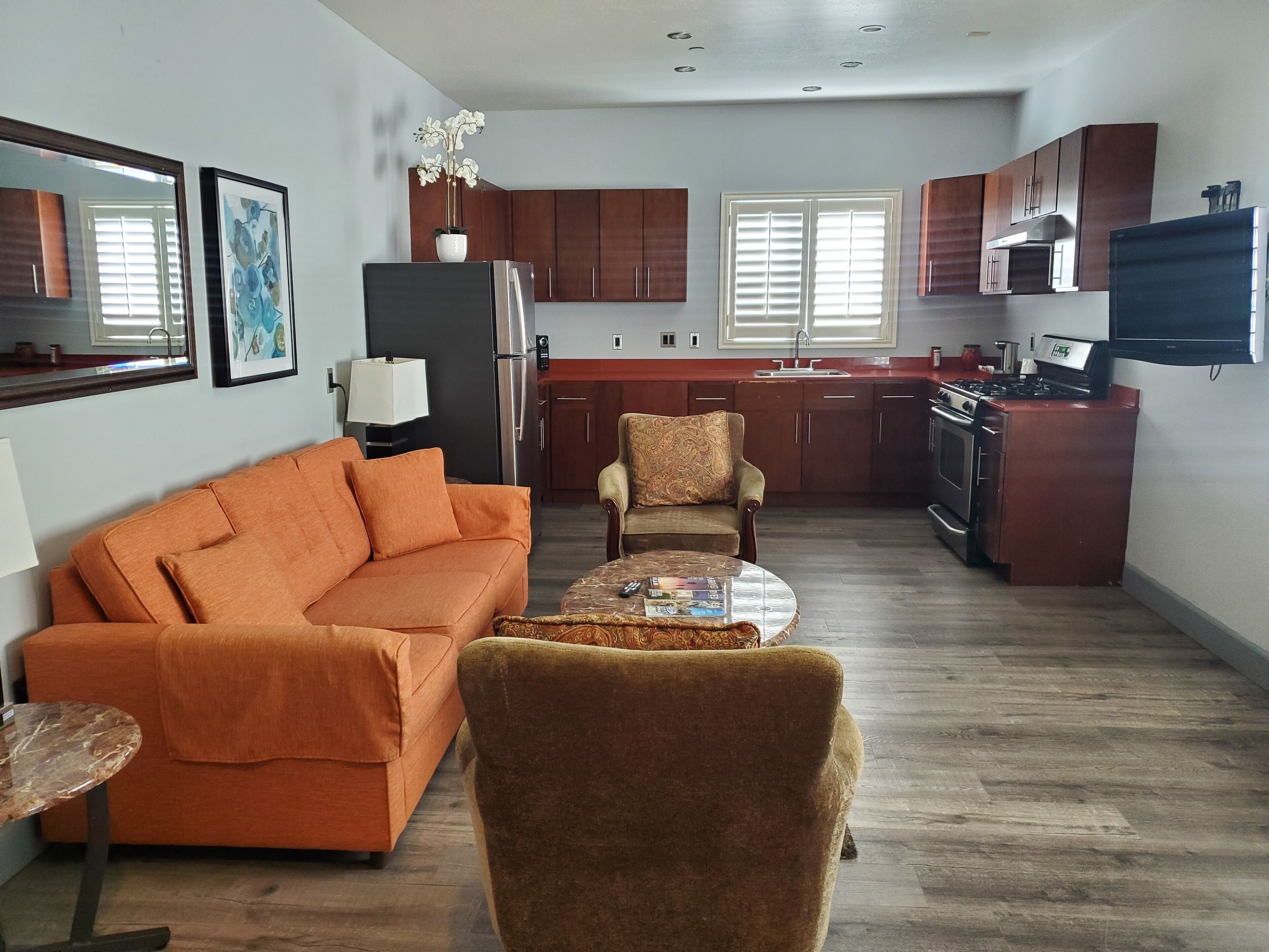 A modern living room with a sofa, armchair, and coffee table. A kitchen with wooden cabinets and appliances is visible in the background.