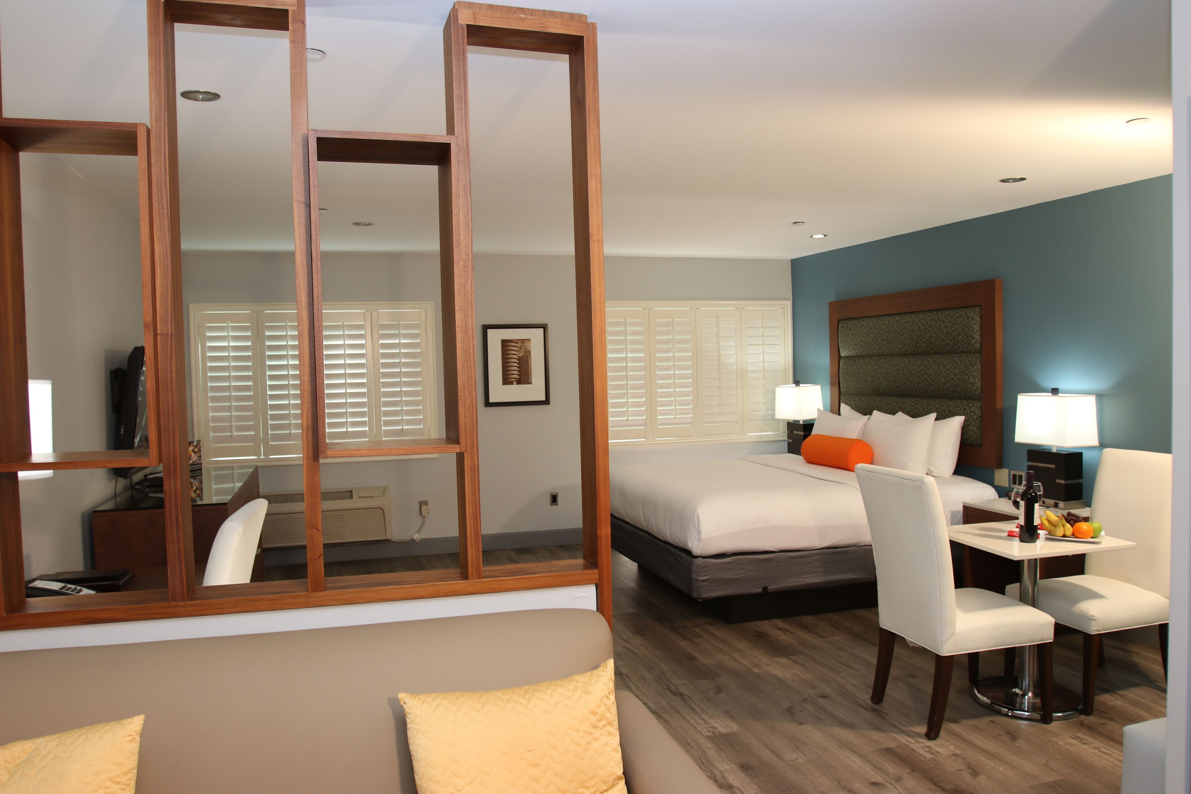 Habitación de hotel con cama, escritorio, silla, sofá, espejo y ventana con persianas.